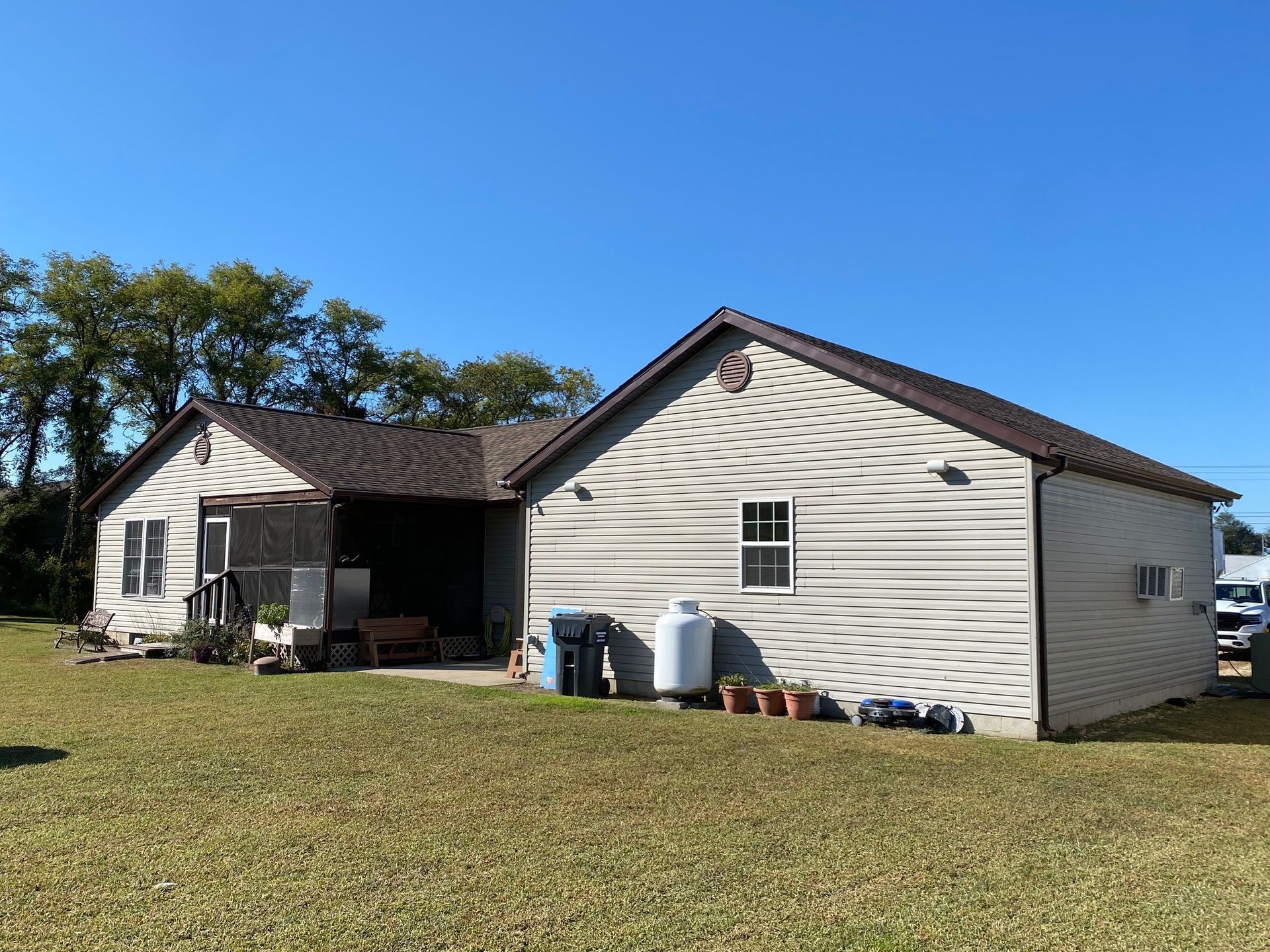 Single-story beige house with white trim and a porch, set on a grassy yard under a clear blue sky