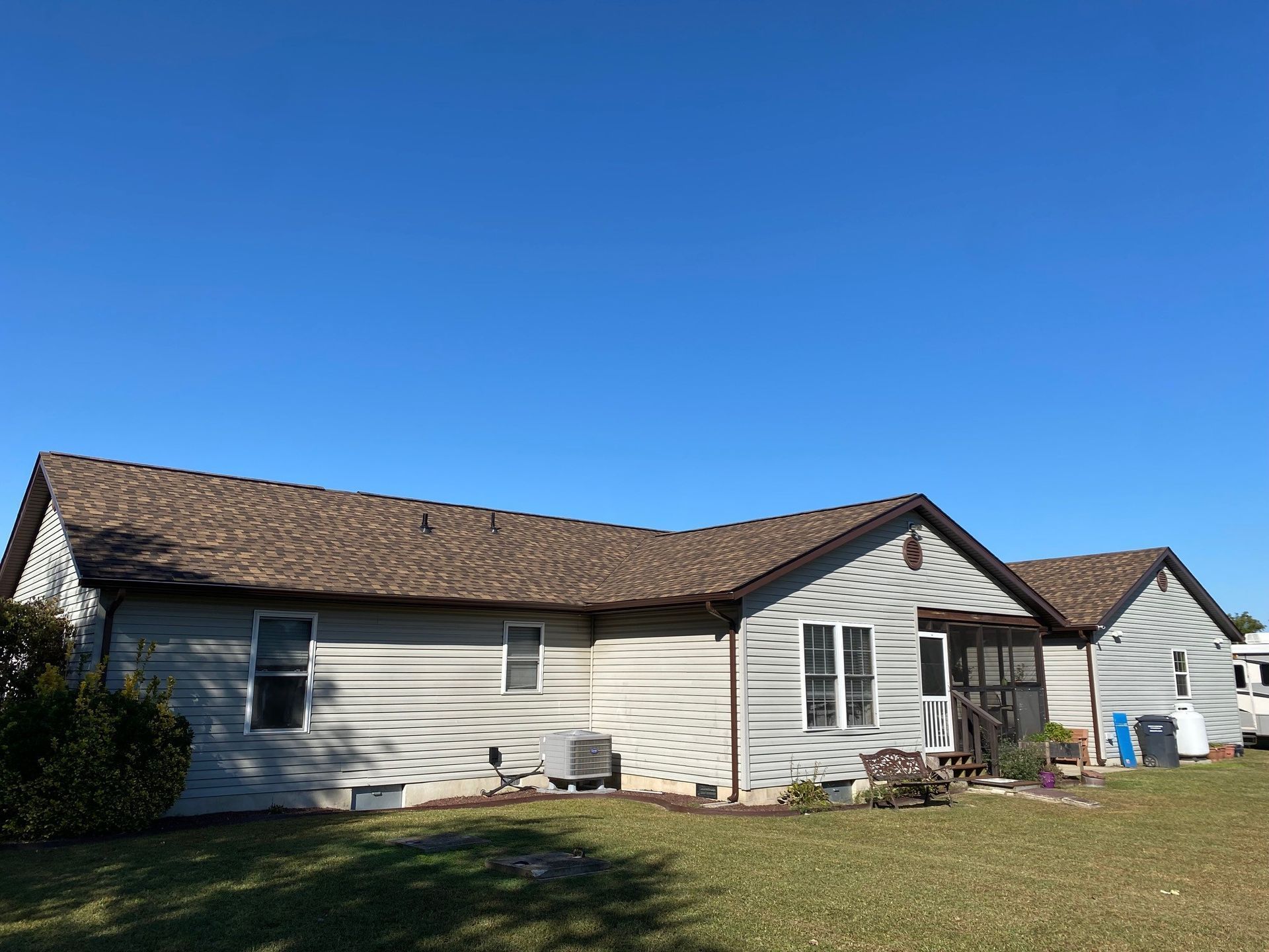 Single-story white house with brown shingle roof under a clear blue sky