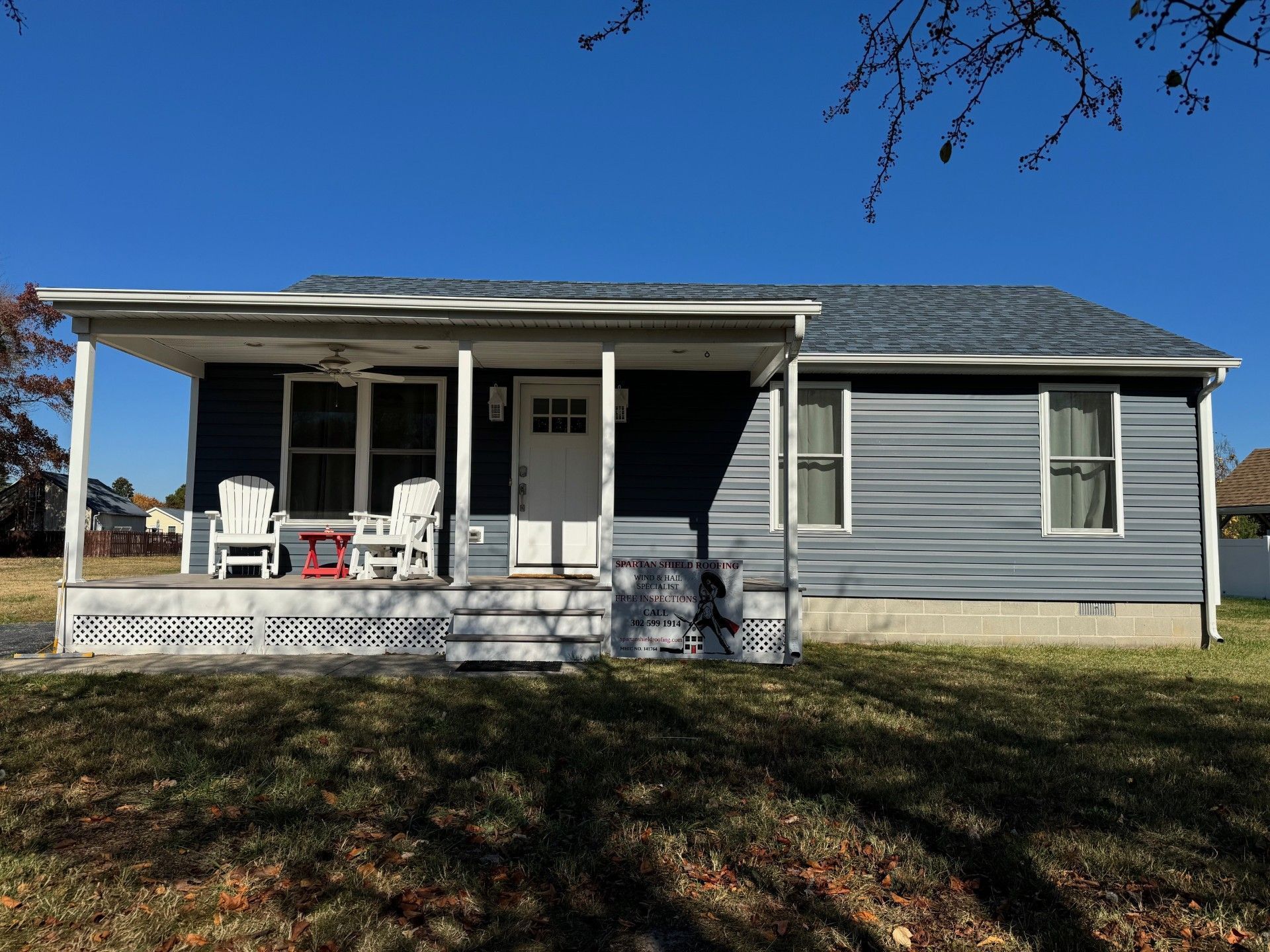 Gray single-story house with a front porch, white trim, and a small set of steps under a blue sky.