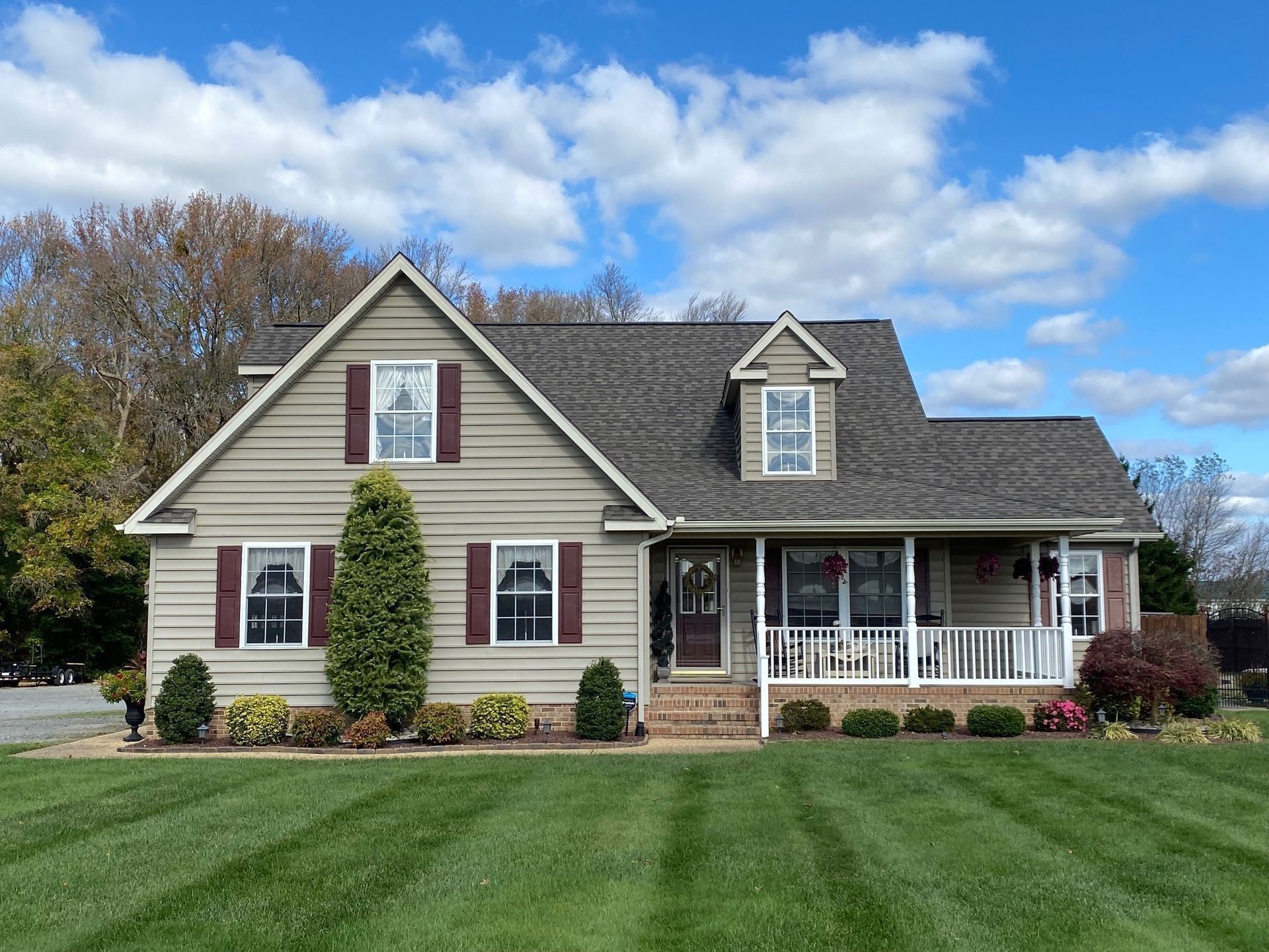 Suburban house with beige siding, white porch, and a manicured lawn under a blue sky