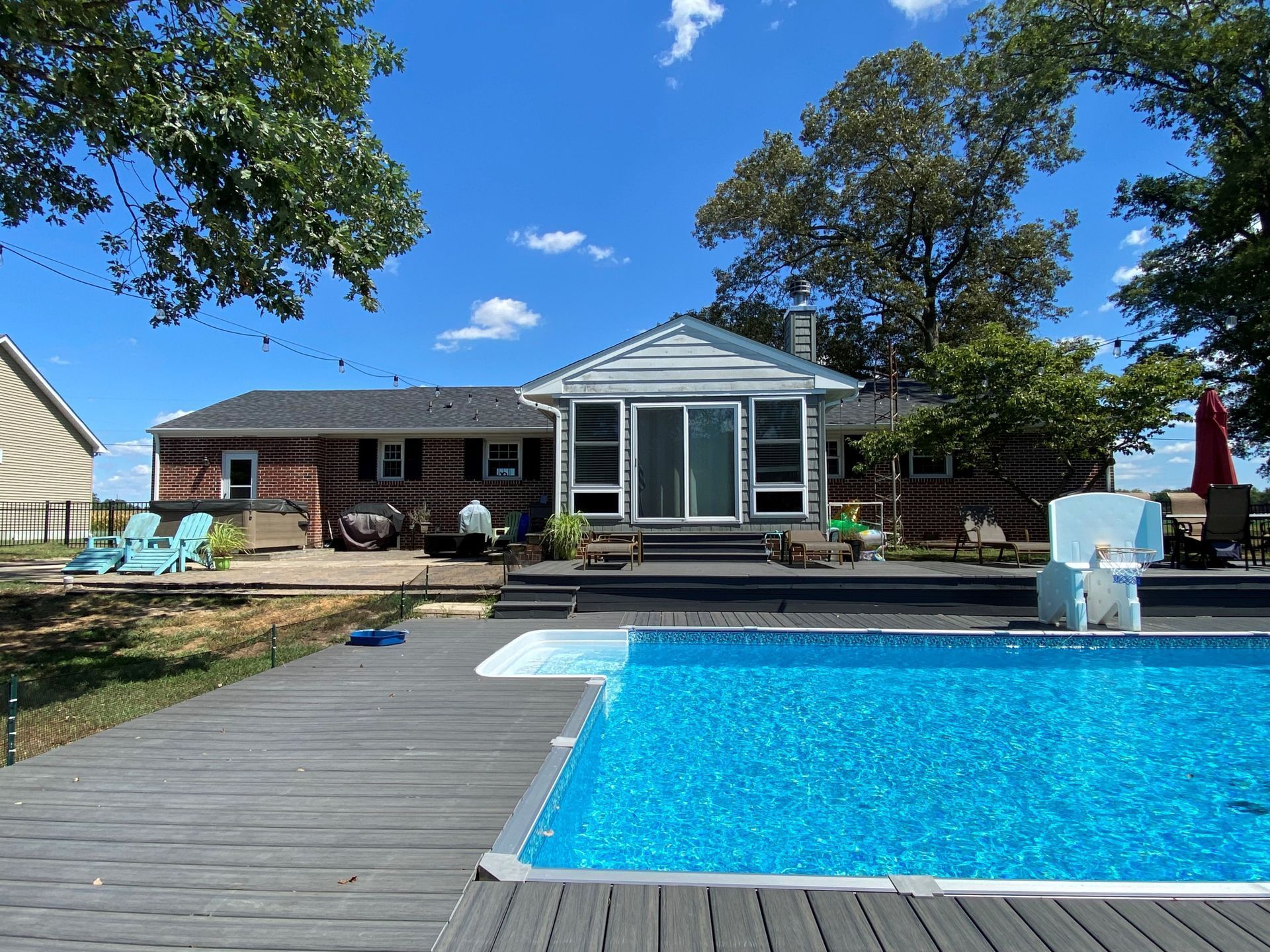 Backyard with a swimming pool, wooden deck, and a house under a blue sky