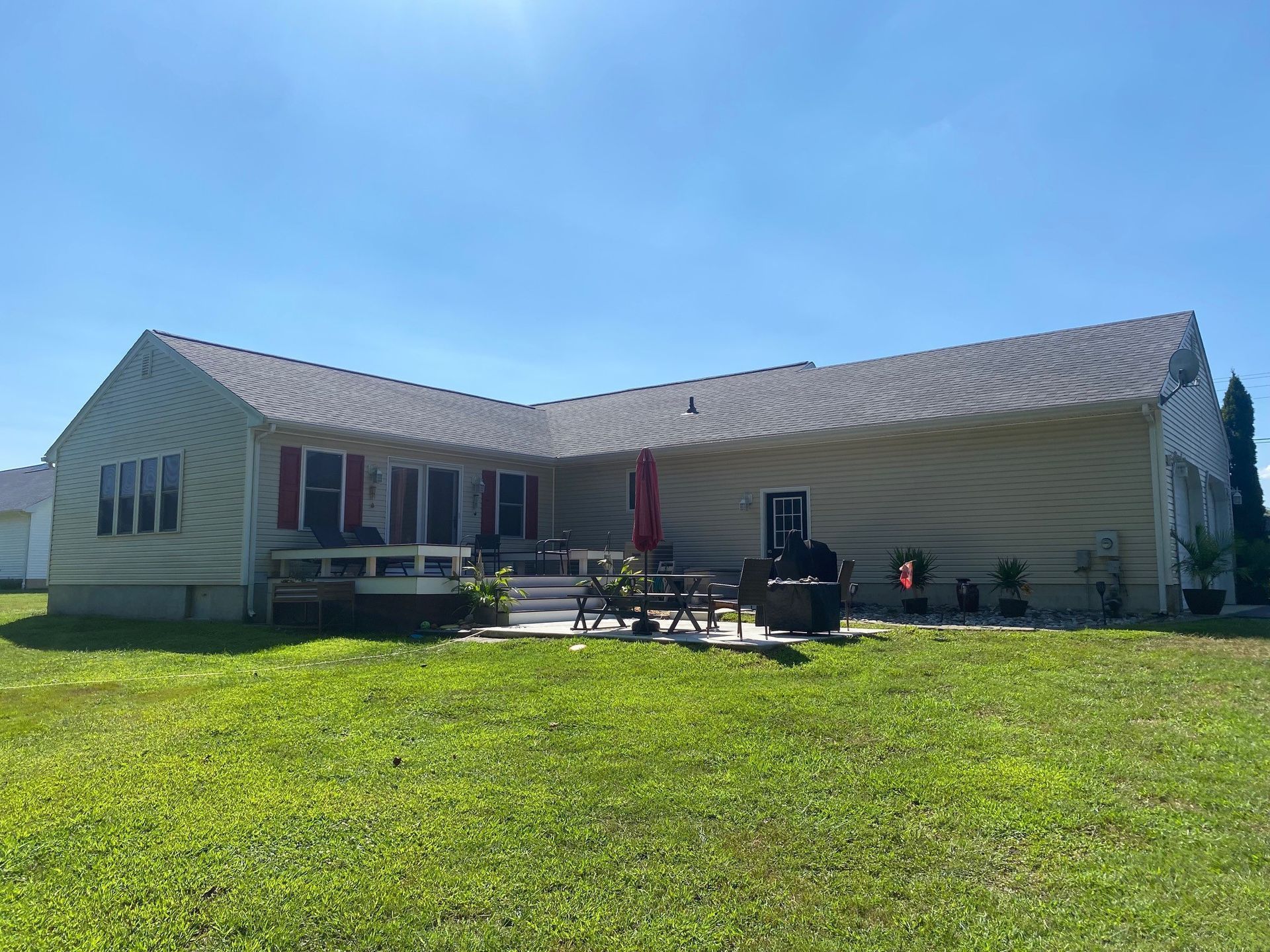 Single-story house with a covered porch, metal roof, and green lawn under a blue sky.