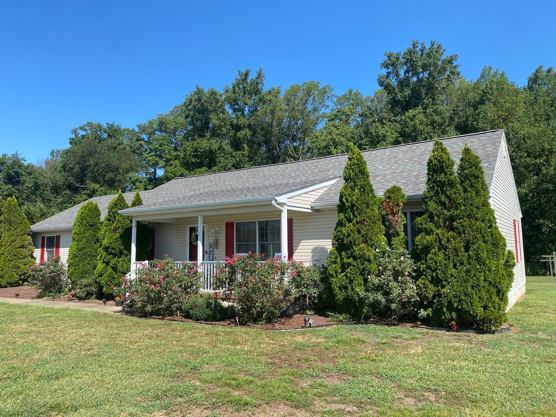 Single-story white house with a front porch, red shutters, and neatly landscaped lawn under a blue sky