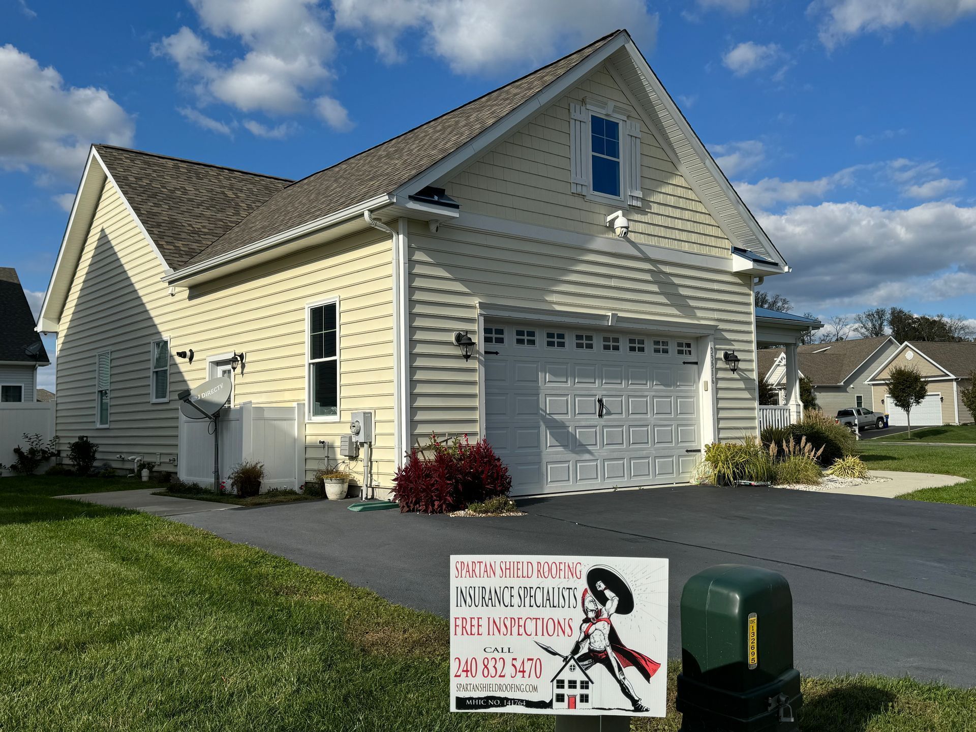 Yellow house with white garage, green lawn, and a driveway sign under a blue sky.