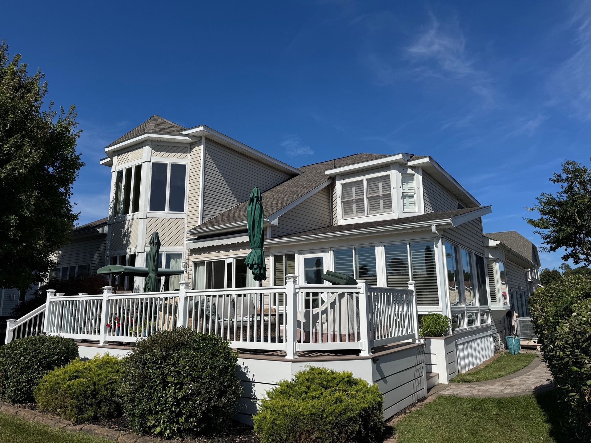 Coastal-style white house with a wraparound porch and railings under a bright blue sky
