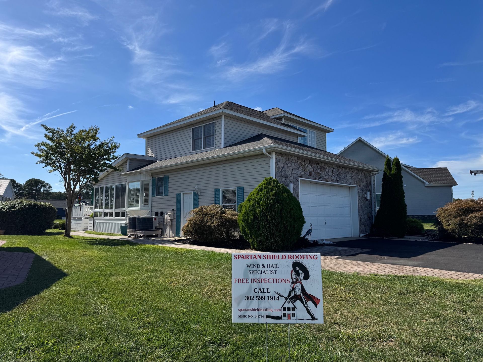Suburban house with garage and porch on a sunny day, with a lawn sign in the front yard