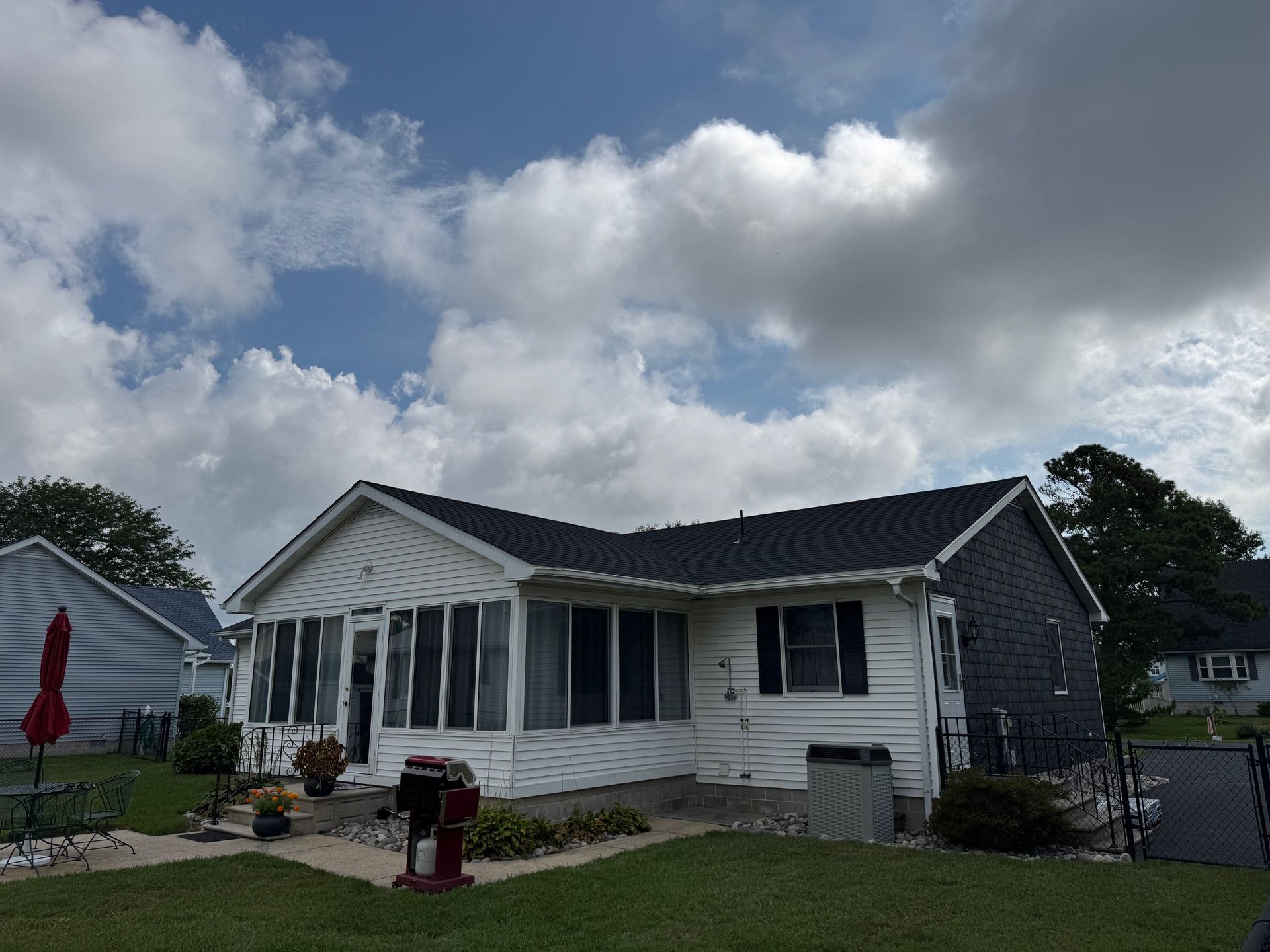 Single-story white house with dark roof and screened porch under a cloudy sky