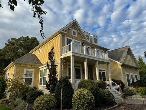 Yellow two-story house with white trim, porch, and dormer windows under a cloudy sky