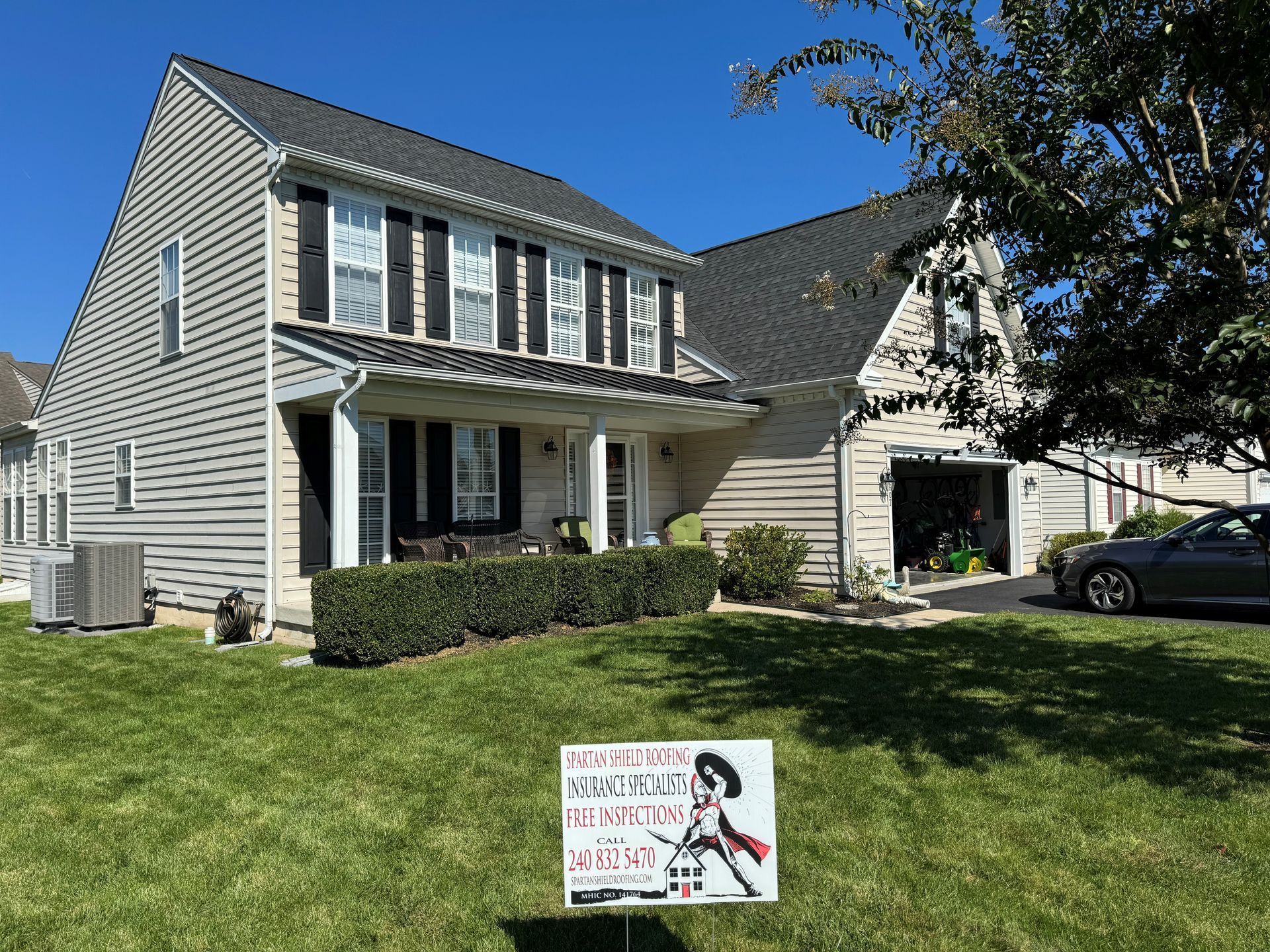 Two-story beige house with a front porch and lawn, with a yard sign in the foreground.