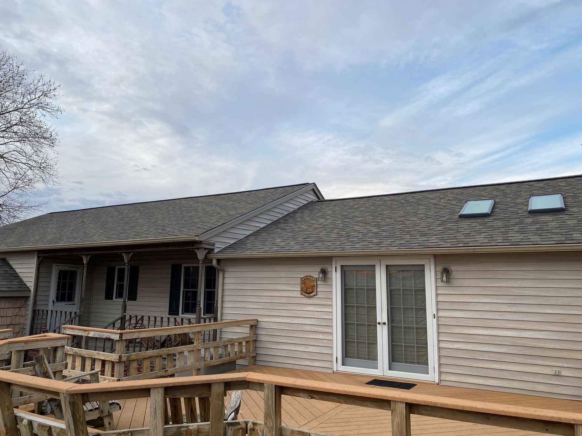 Back deck and patio of a beige house with a shingled roof and cloudy sky