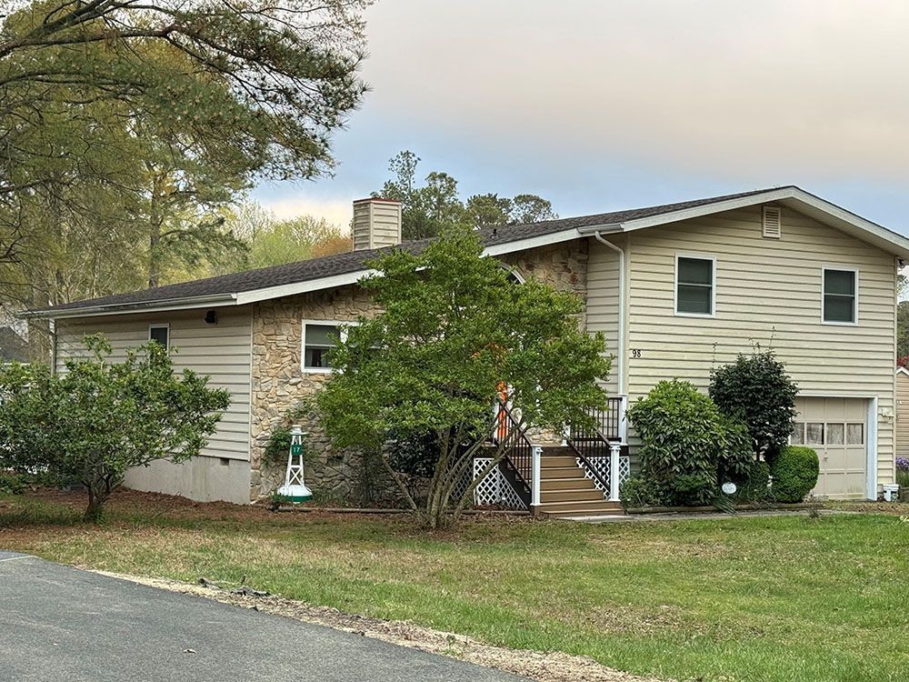 Beige two-story suburban house with trees and lawn beside a road