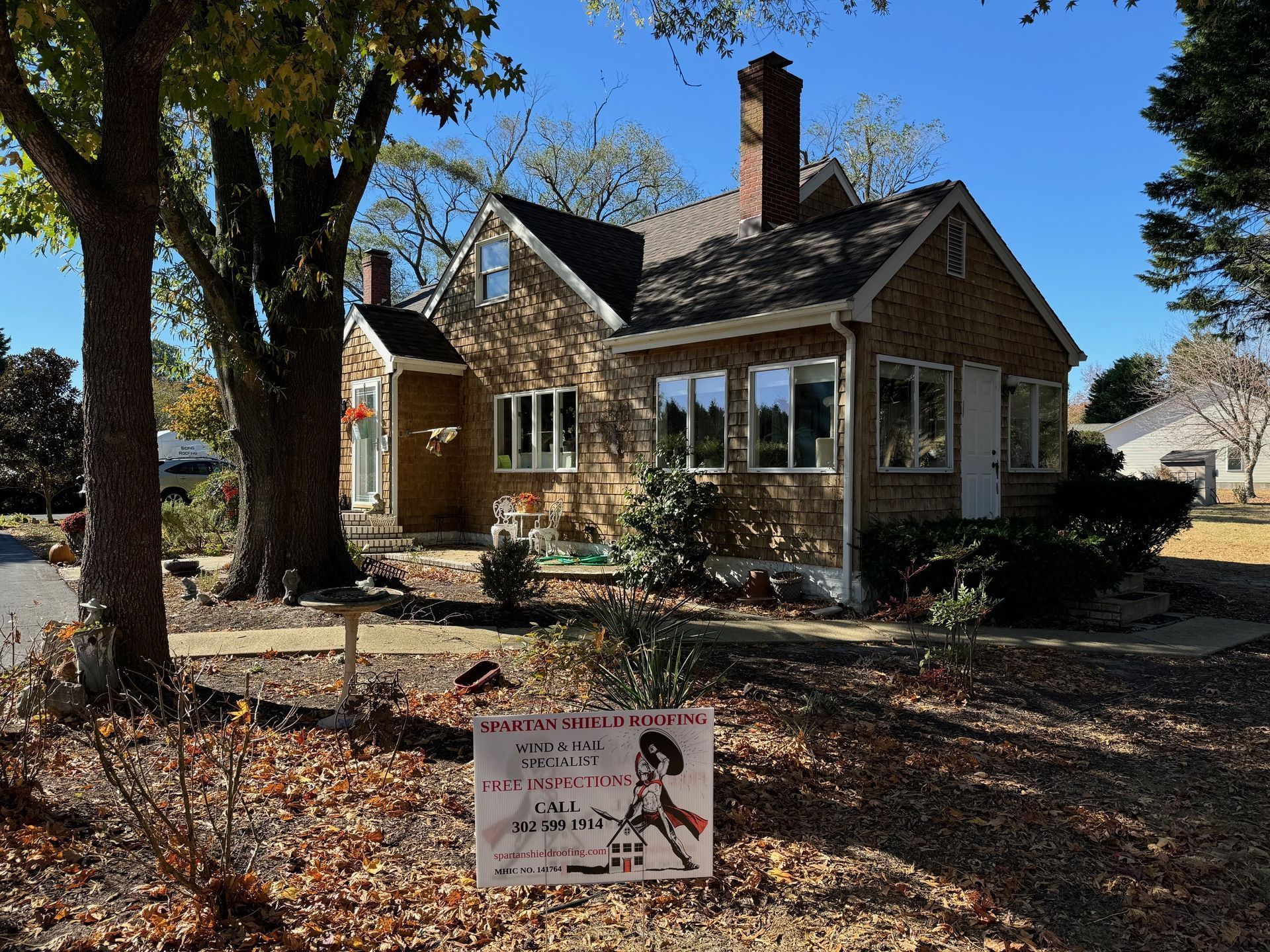 Brick house with a chimney and yard sign under large trees on a sunny day