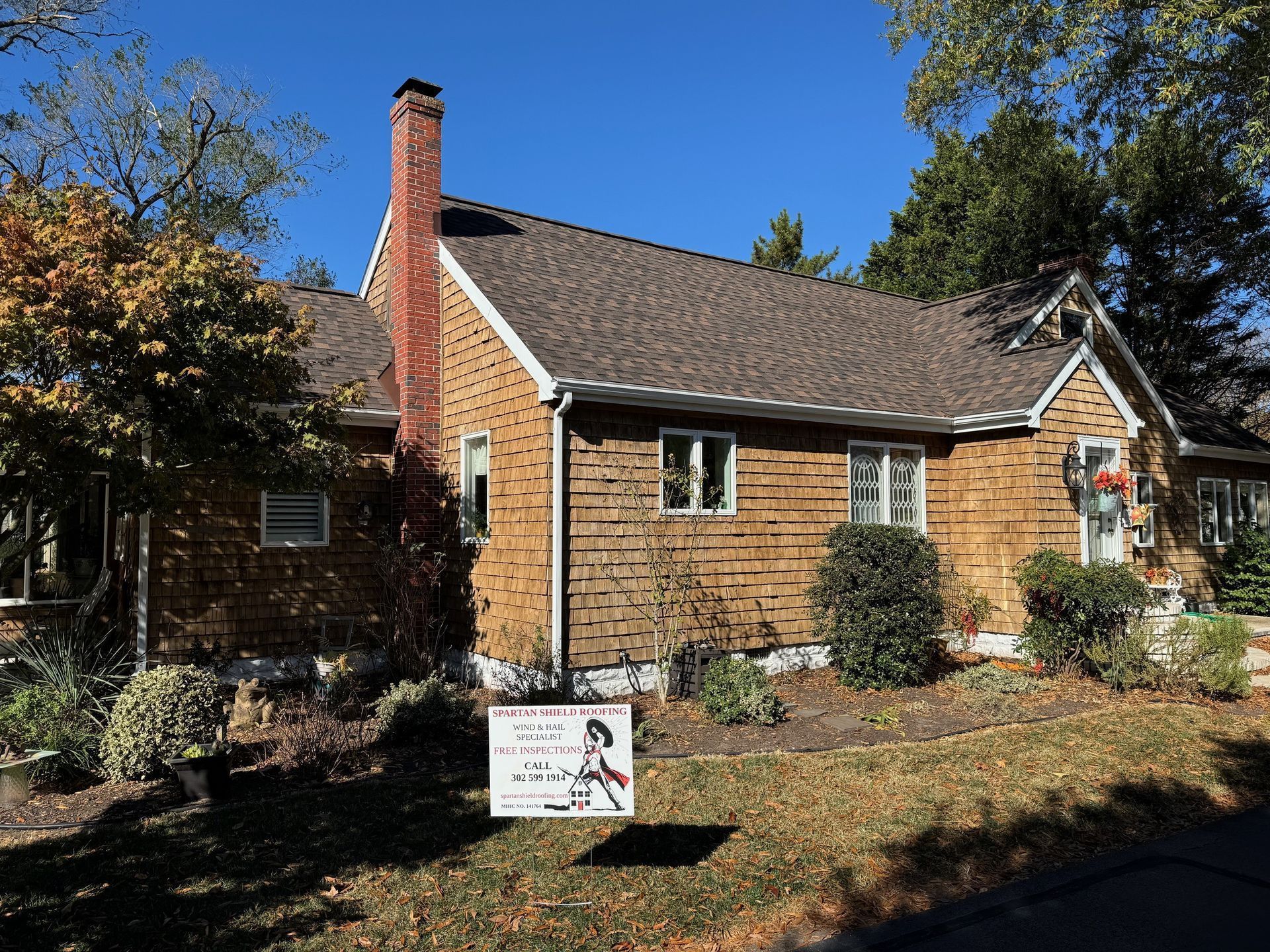 Brick house with chimney, front yard, and a small yard sign in sunlight