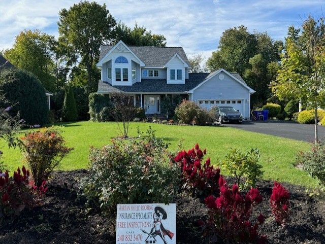 Suburban house with manicured lawn, flowering shrubs, and driveway under a bright blue sky