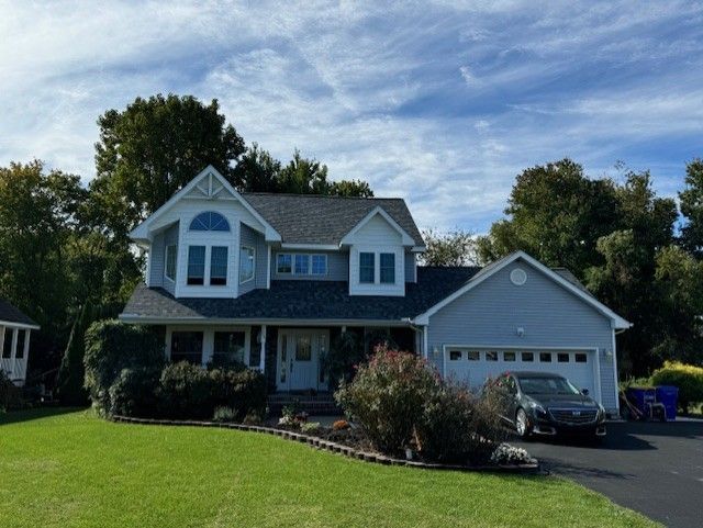 Suburban gray two-story house with white trim, front lawn, driveway, and attached garage under a blue sky