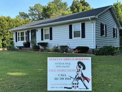 White house with black shutters and a roofing company sign in the front yard