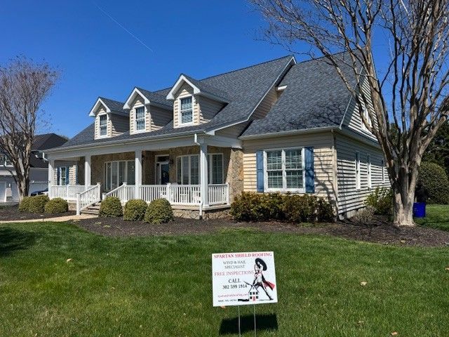 Suburban house with gray siding, white porch, and lawn sign in the front yard on a sunny day