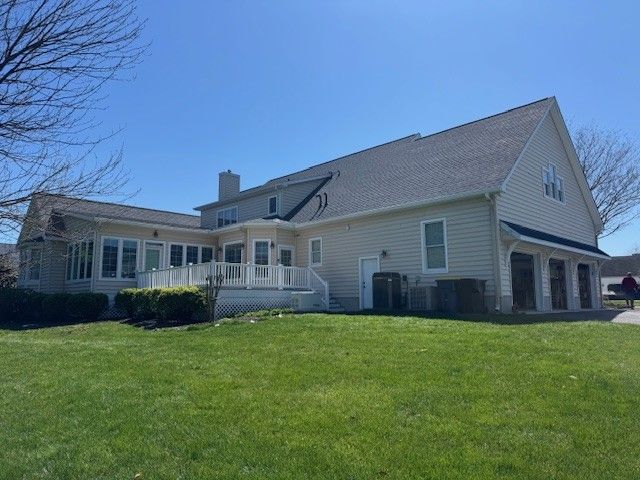 Large beige house with white trim, screened porch, and a green lawn under a blue sky