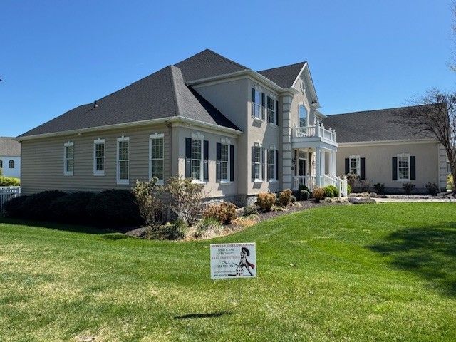 Suburban house with gray siding, white trim, and manicured lawn under a clear blue sky