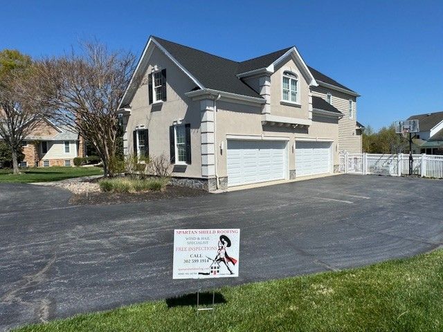 House with two-car garage and for-sale sign beside a paved driveway on a sunny day