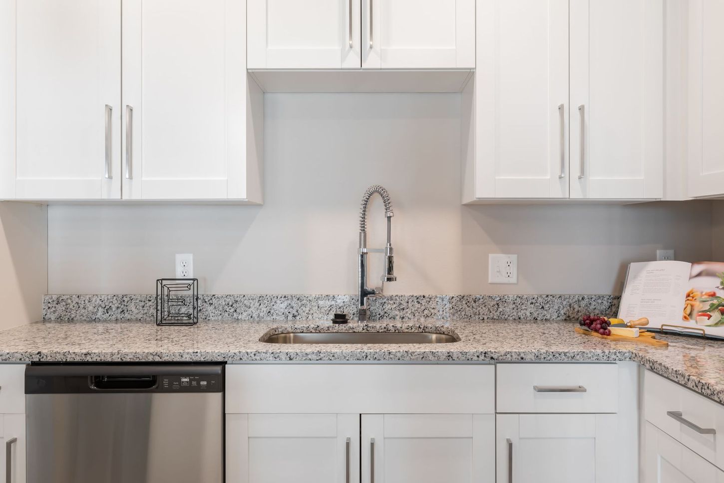 A kitchen with white cabinets , granite counter tops , a sink , and a stainless steel dishwasher.