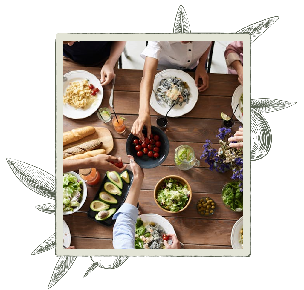 People at a wooden table sharing a meal with pasta, salad, and bread.