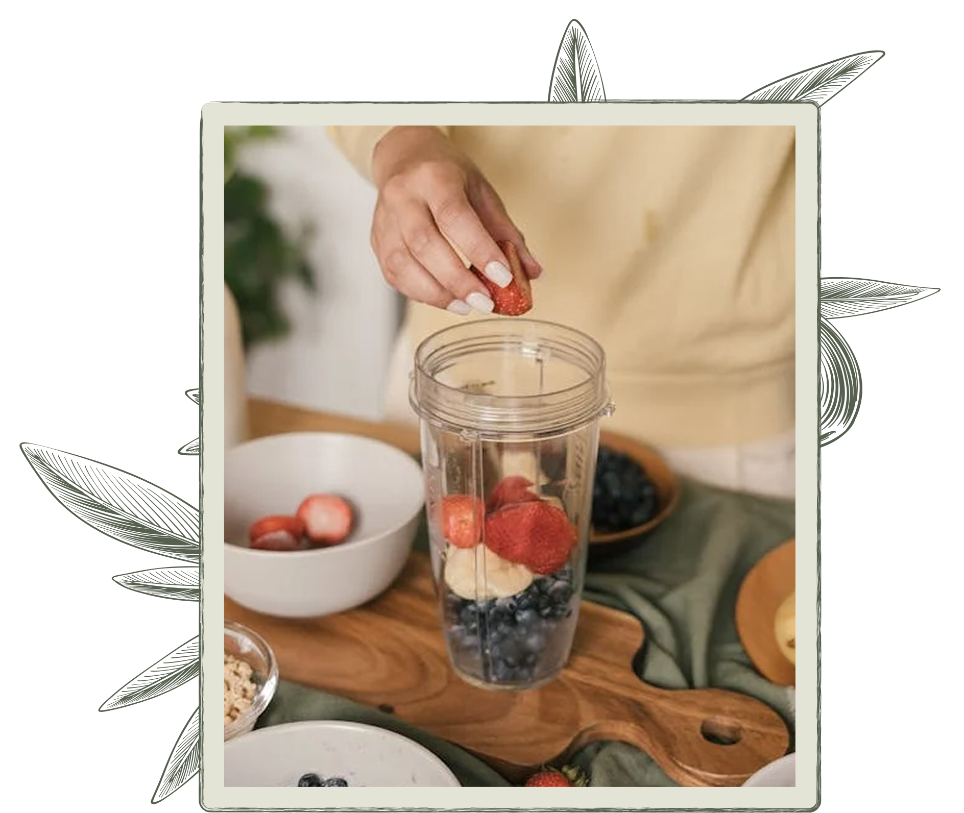 Person adding strawberry to a blender filled with fruit on a wooden board.