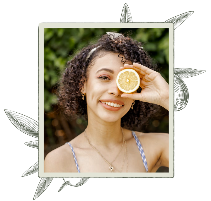 Woman holding a lemon slice to her eye, smiling. Outdoors.