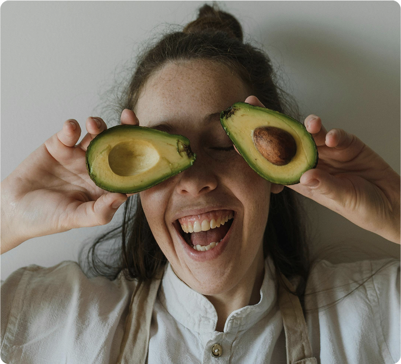 Woman holding avocado halves over her eyes, smiling widely.