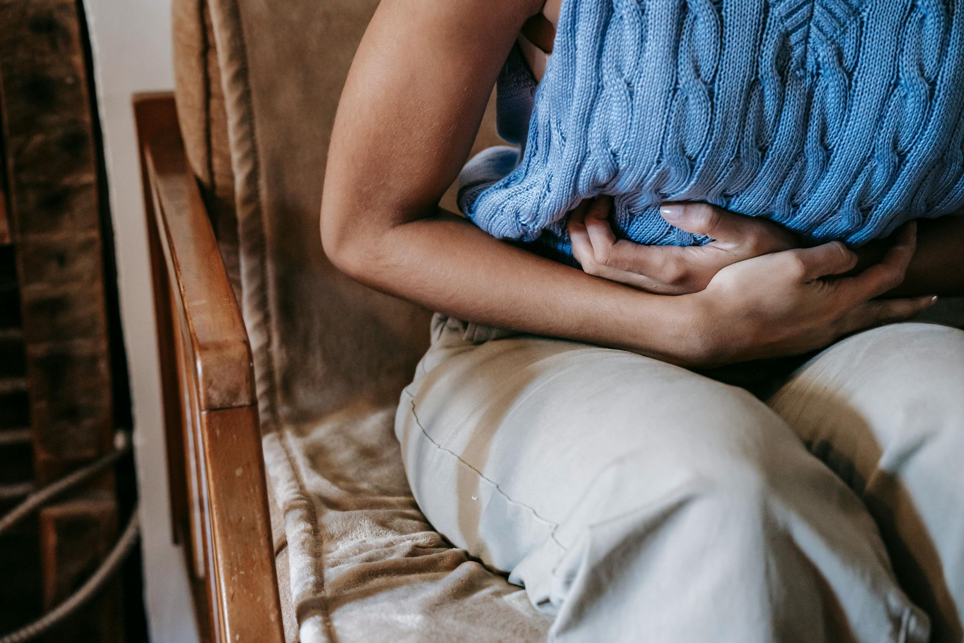 Person holding a blue knitted blanket over their lap while sitting on a beige chair