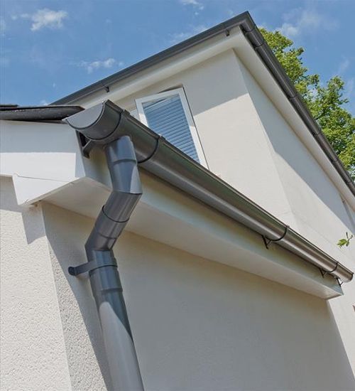 White house corner with gray gutters and downspout against a blue sky