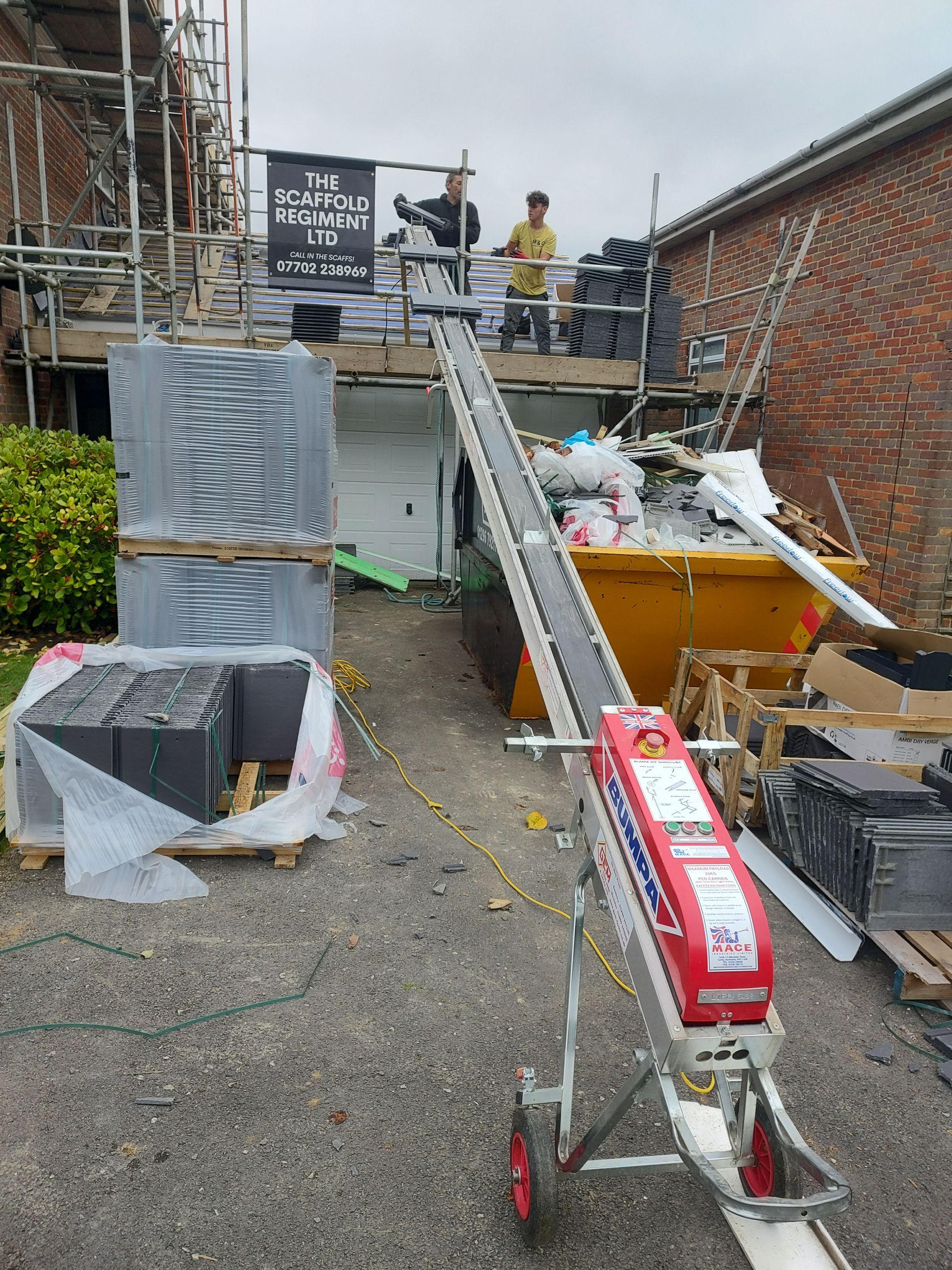 Rubble-filled construction site with a slanted metal ramp, scaffolding, bins, and workers in the background