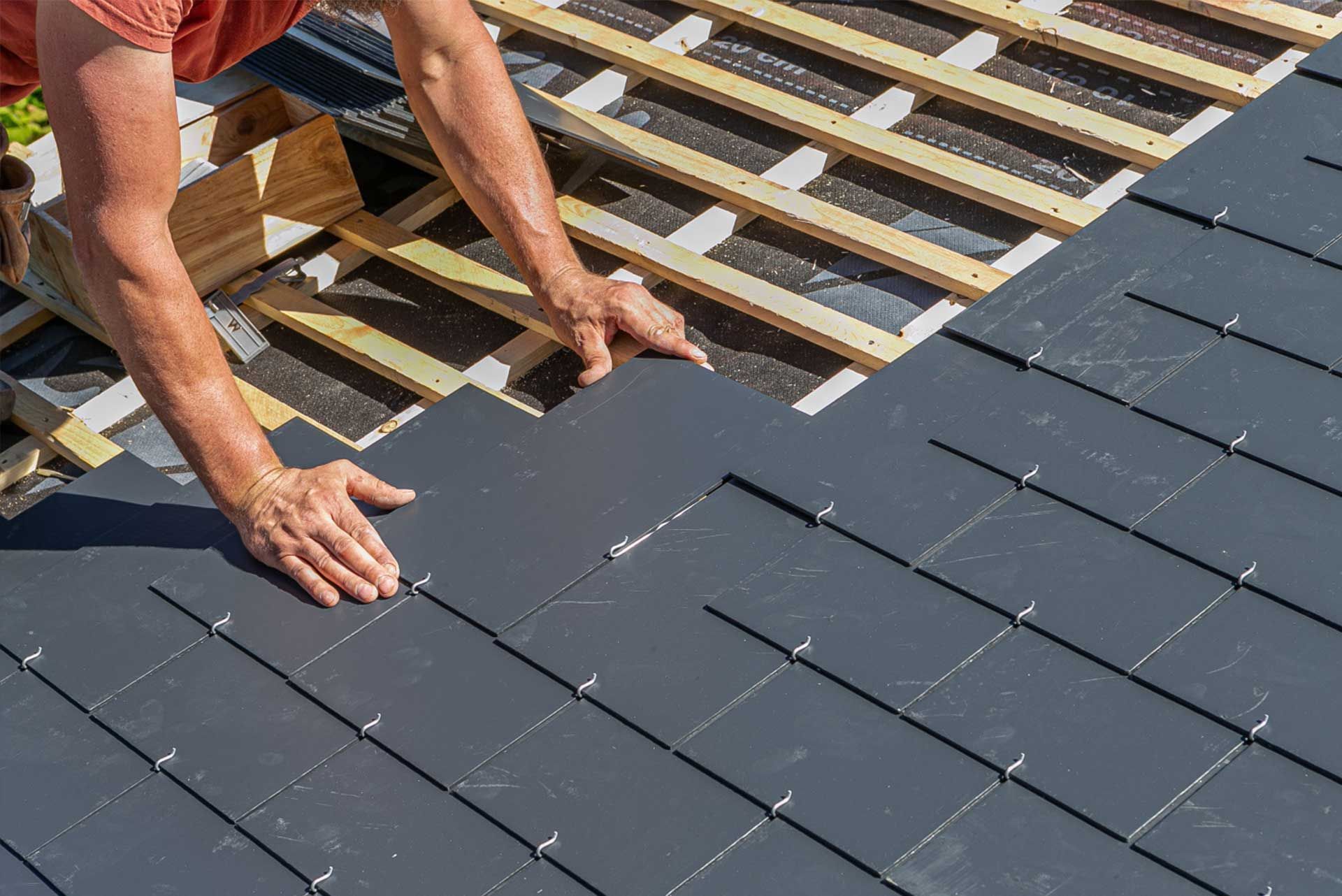 Worker installing dark roof shingles on a house roof frame
