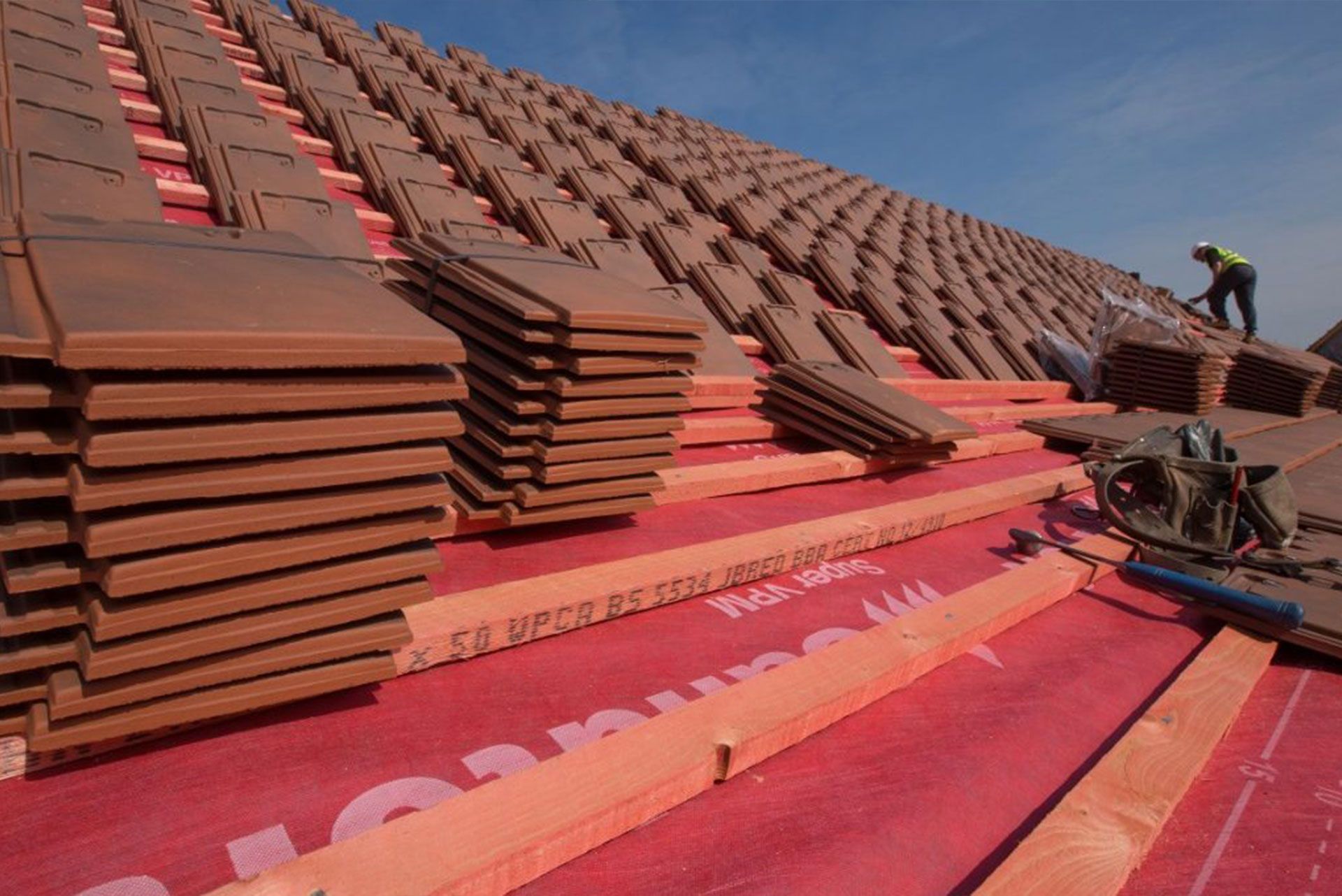 Workers installing roof tiles on a steep red-roofed building under construction