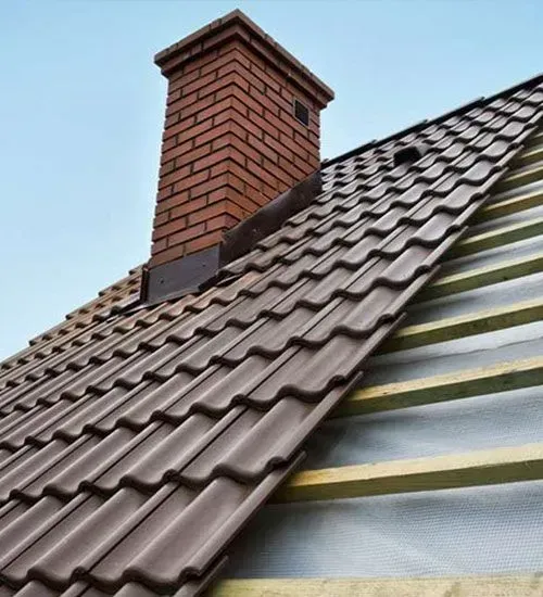 Brick chimney on a dark brown tiled roof with underlayment visible on the right side.