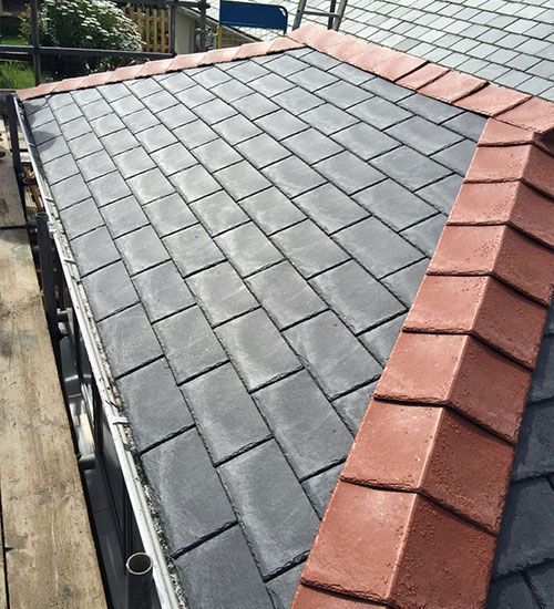 Roof with dark gray shingles and a red ridge cap, showing a steep sloped residential roof.