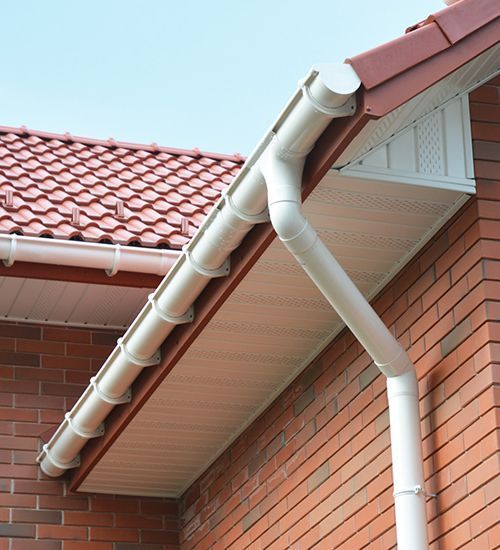White rain gutters and downspout on a red brick house with a tiled roof