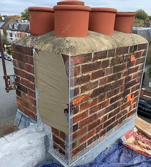 Brick chimney with four red flue pots on a rooftop, one side patched with gray mortar or sealant