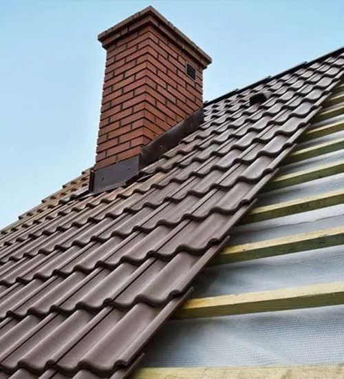 Close-up of a sloped roof with brown tiles and a brick chimney against a blue sky