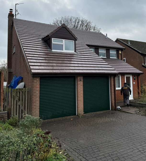Brick house with green garage doors and a person at the front door under a cloudy sky