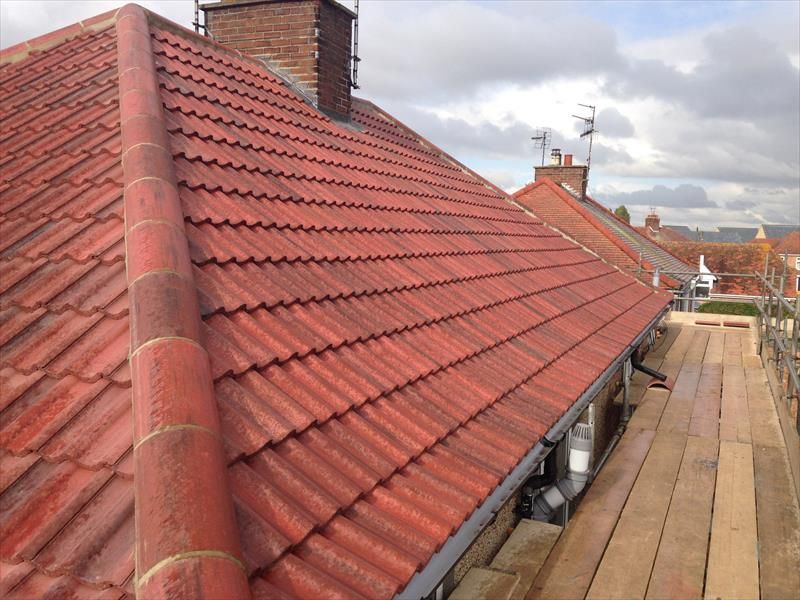 Red tiled roof with chimney and wooden walkway on a sloped building under a cloudy sky