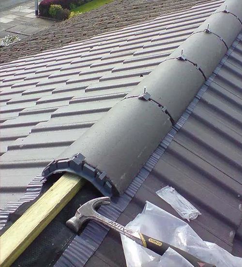Roofing work on a metal roof, with a black ridge vent and tools in the foreground