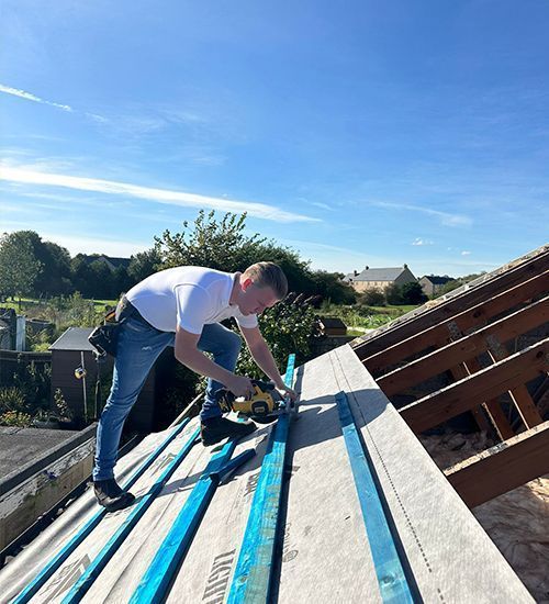 Worker using a circular saw on roof decking under a blue sky