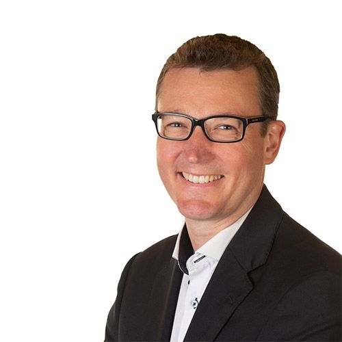 Man in glasses and black suit smiling, white background.