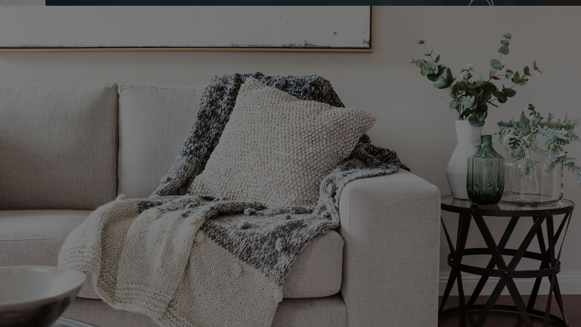 Beige couch with textured throw, decorative pillow, and vase of eucalyptus.