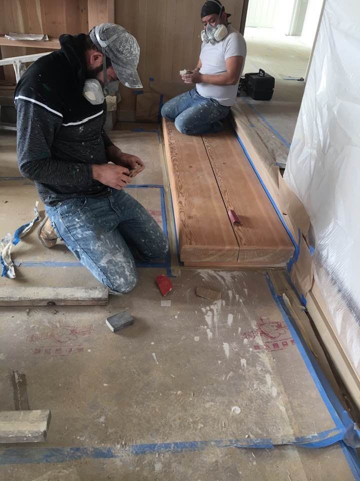 Two men are working on a wooden bench in a room.