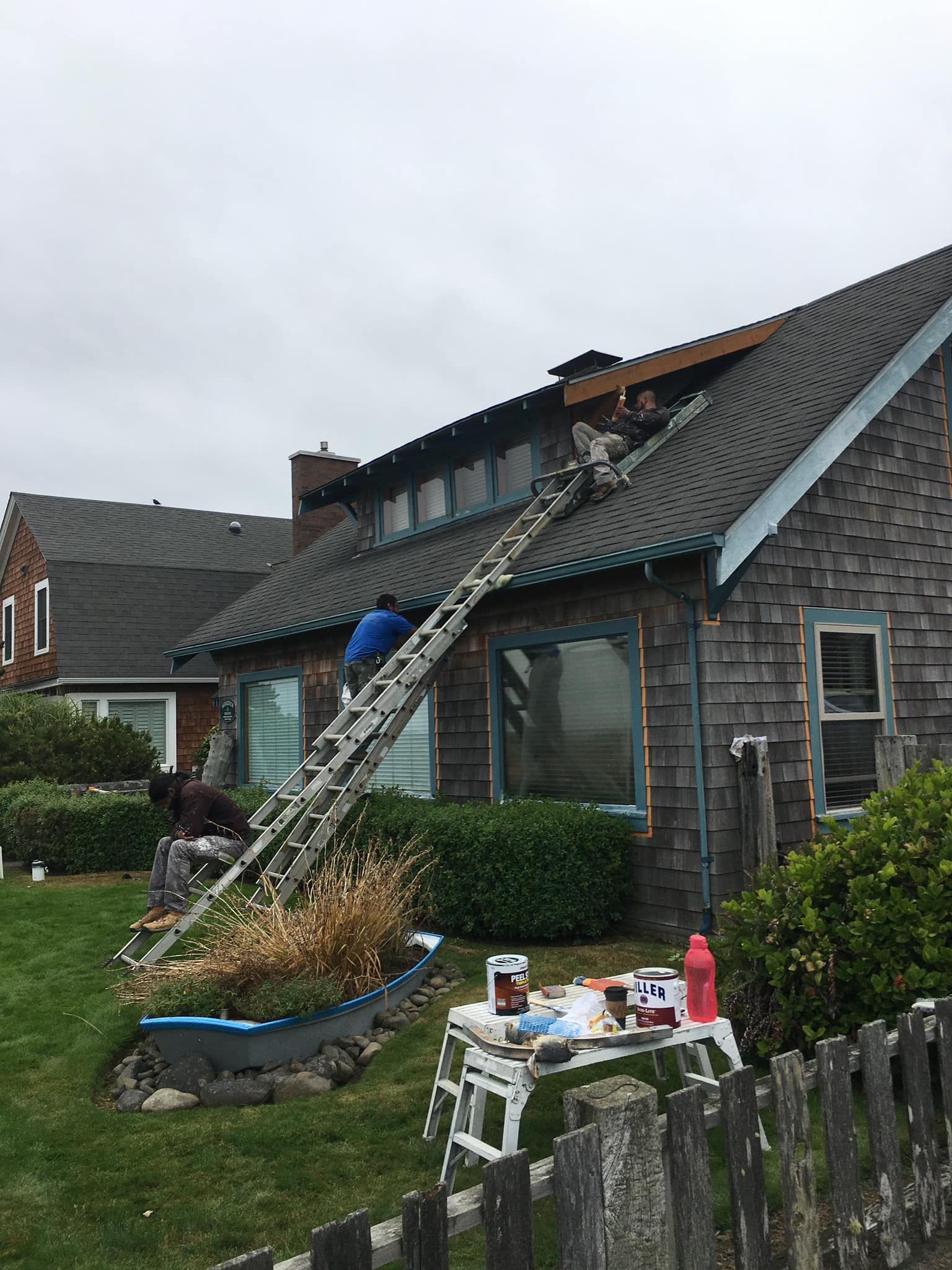 A man on a ladder is painting the roof of a house.