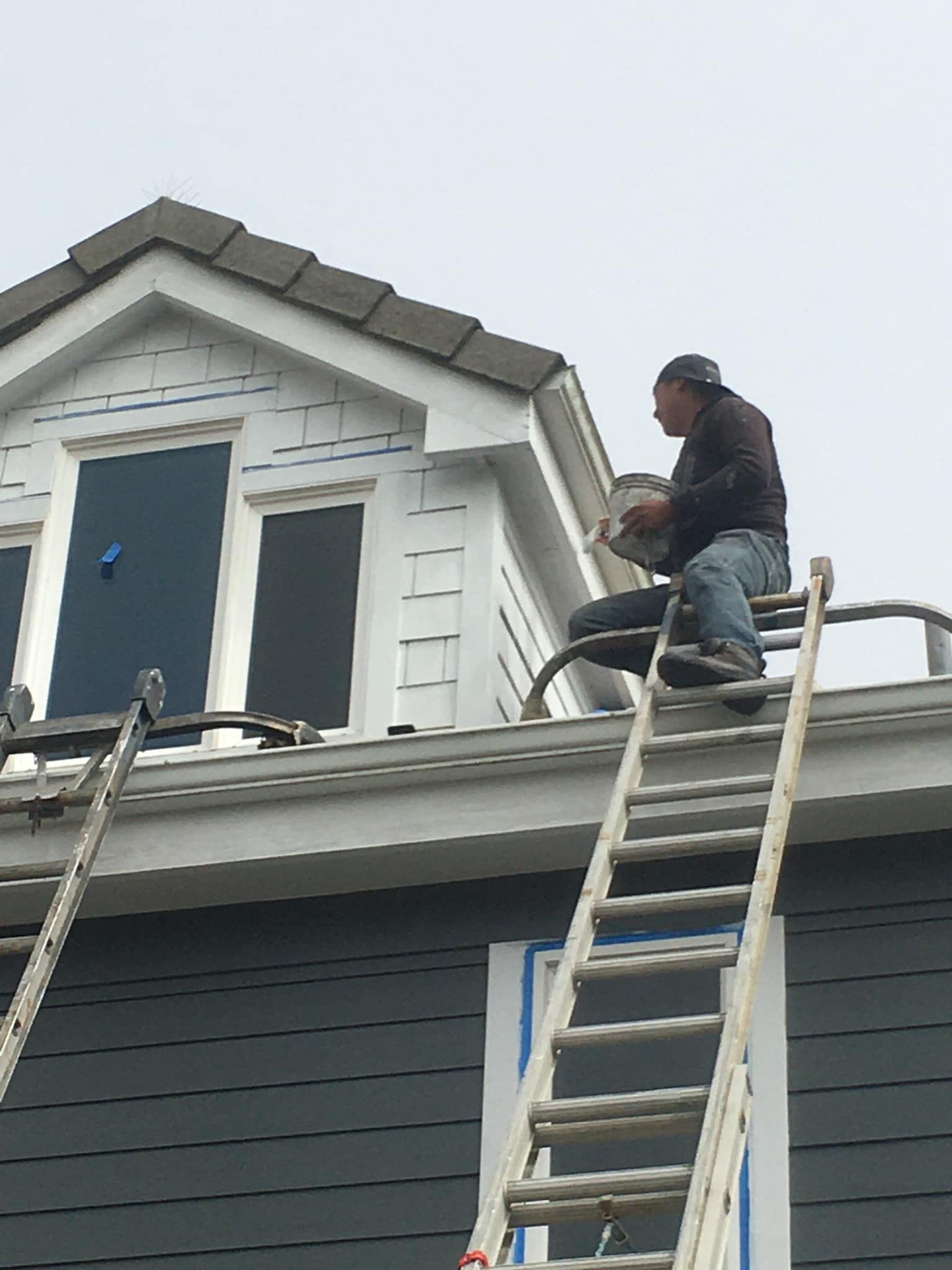 A man is sitting on a ladder on the roof of a house.