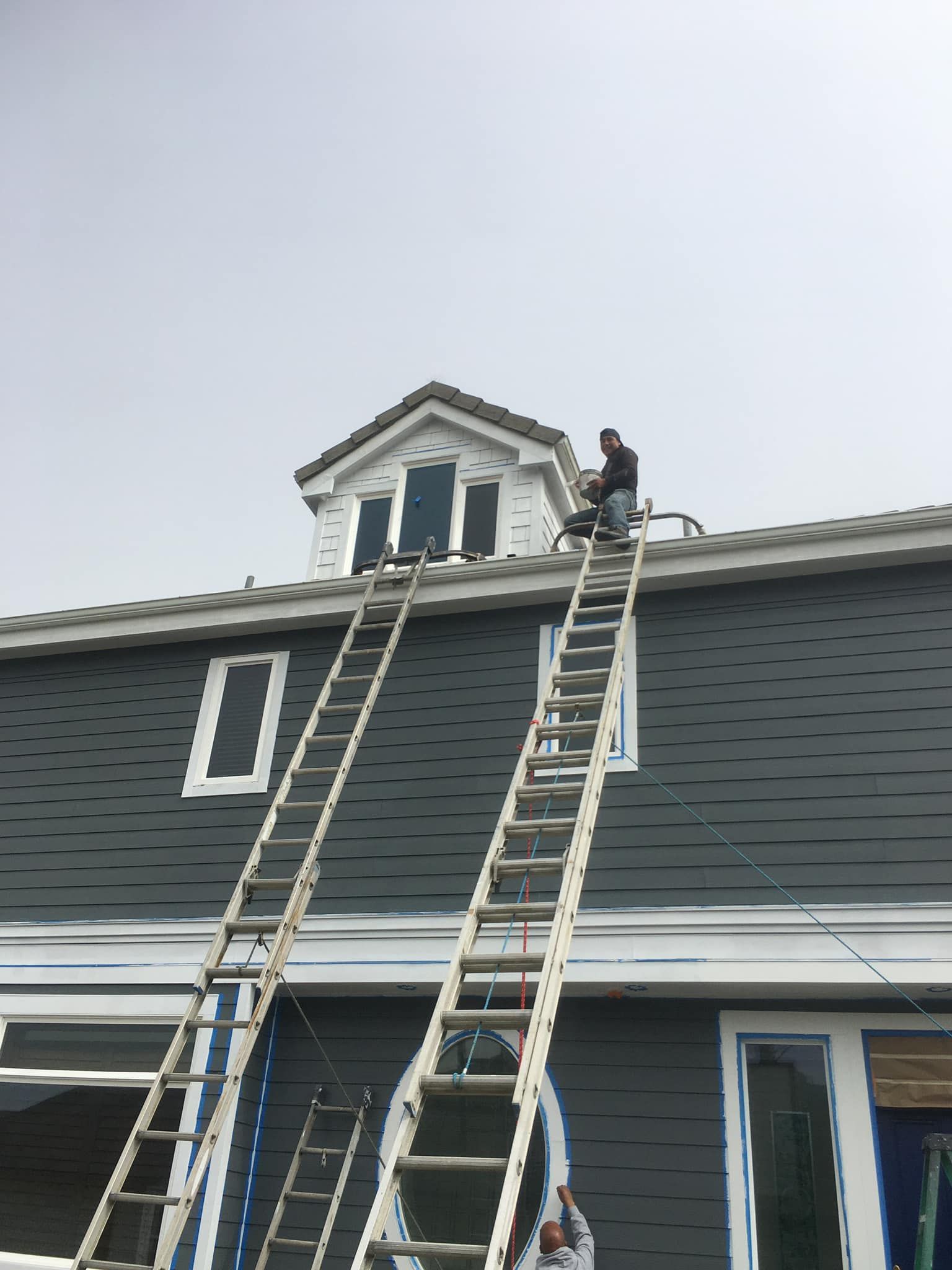 A man is sitting on a ladder on the roof of a house.