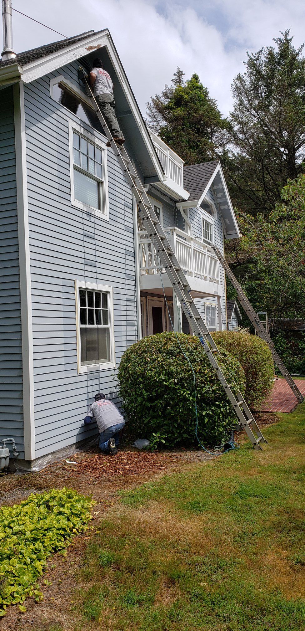 A man is painting the side of a house with a ladder.
